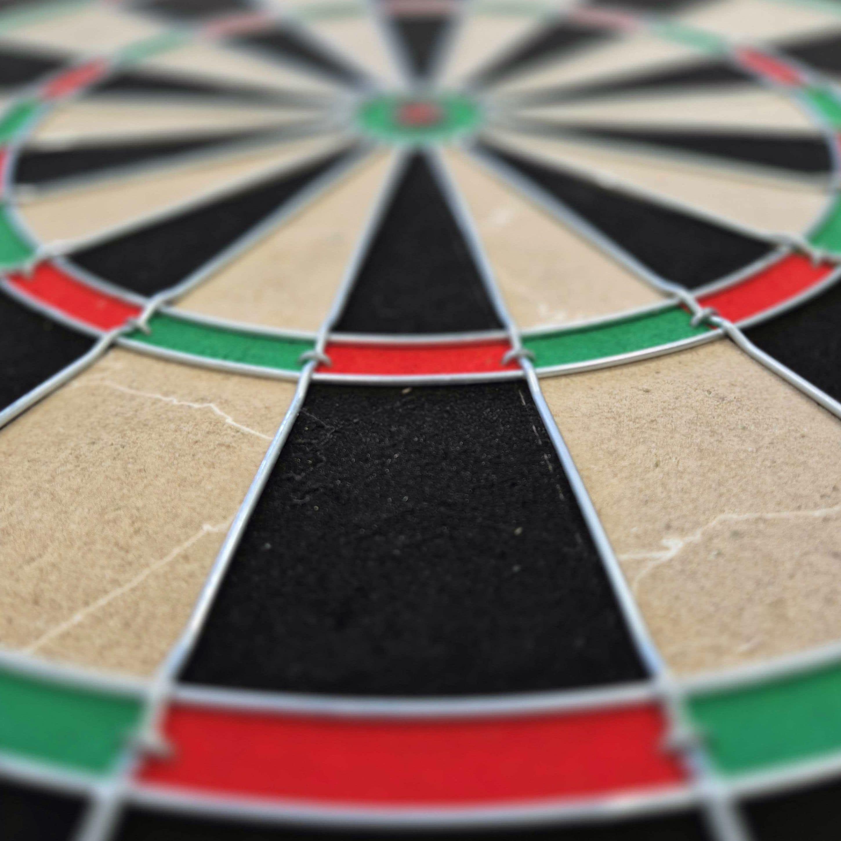 Target Dimitri Van Den Bergh Steeldartboard Set Das Bild zeigt eine Nahaufnahme eines Steeldartboards mit schwarz, beige, rot und grün markierten Segmenten. Besonders gut zu erkennen sind die Drähte, die die Felder voneinander trennen.