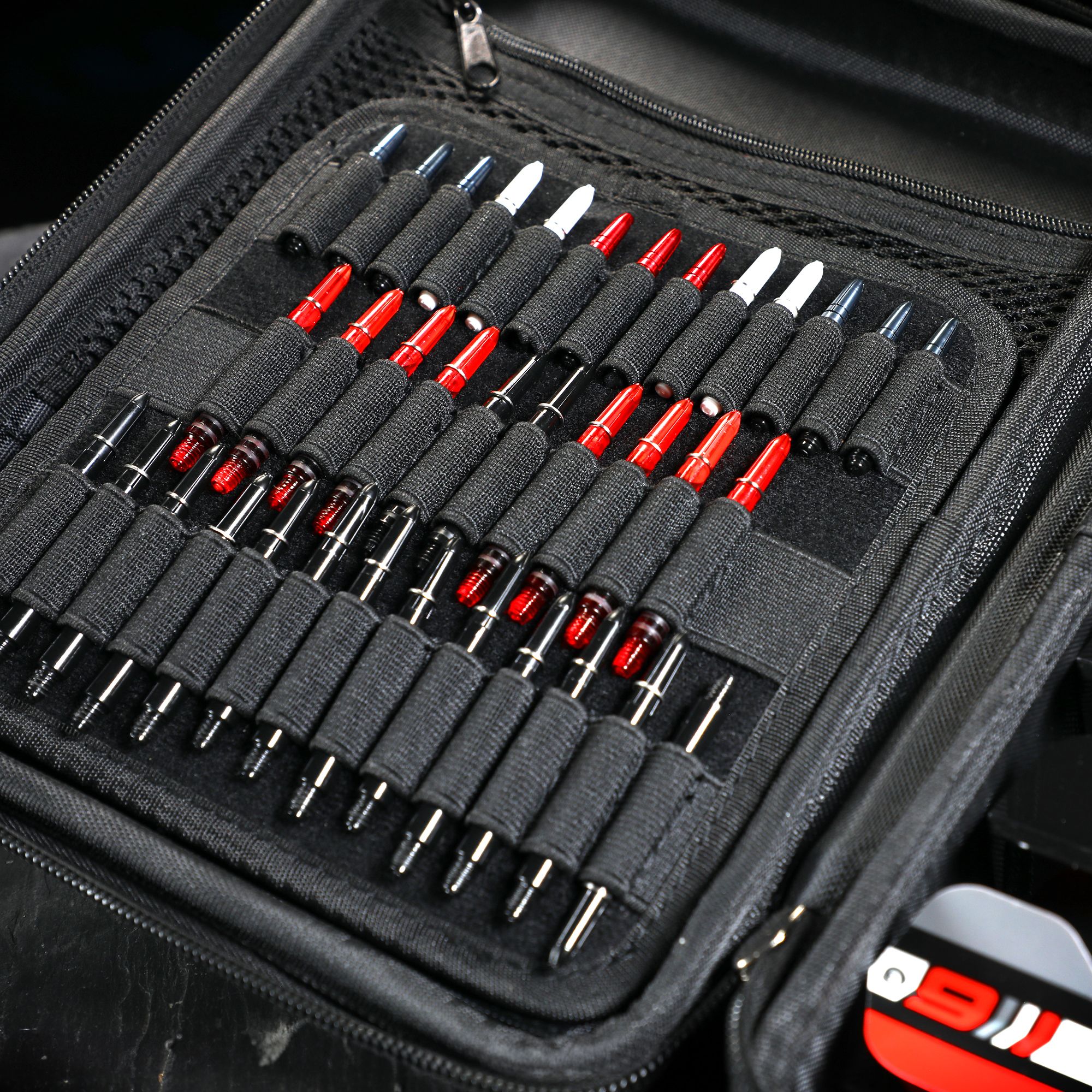 In diesem Bild sieht man ein Dart-Etui mit zahlreichen roten und schwarzen Dartspitzen. Die Spitzen sind ordentlich in elastischen Schlaufen im Inneren des Etuis angeordnet.