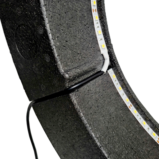 Bulls NL Lumo Light Surround Beleuchtungssystem Das Bild zeigt das „Bulls NL Lumo Light Surround Beleuchtungssystem“ mit LED-Leuchtstreifen auf einer schwarzen, strukturierten Oberfläche. Ein Kabel ist ebenfalls an das Beleuchtungssystem angeschlossen.